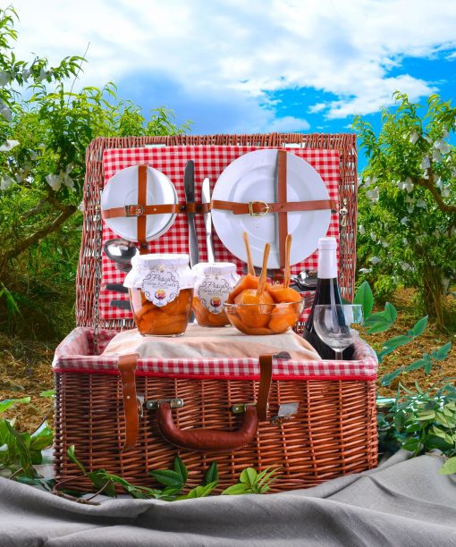 Un vero cesto da picnic vintage con piatti, posate, confetture di pesche e vino su una tovaglia distesa all'ombra di un pescheto.